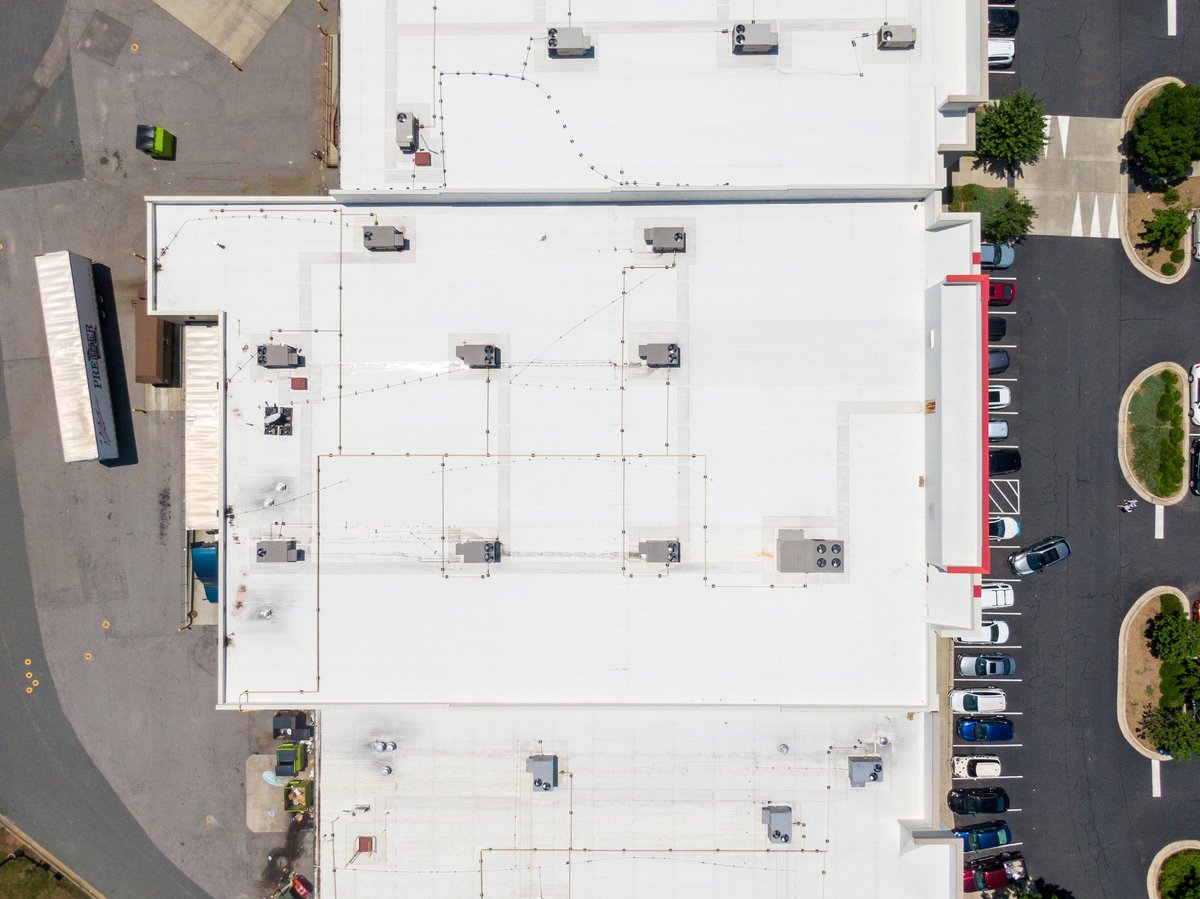 A comprehensive aerial view of a commercial facility with white TPO flat roofing membrane and rooftop HVAC units
