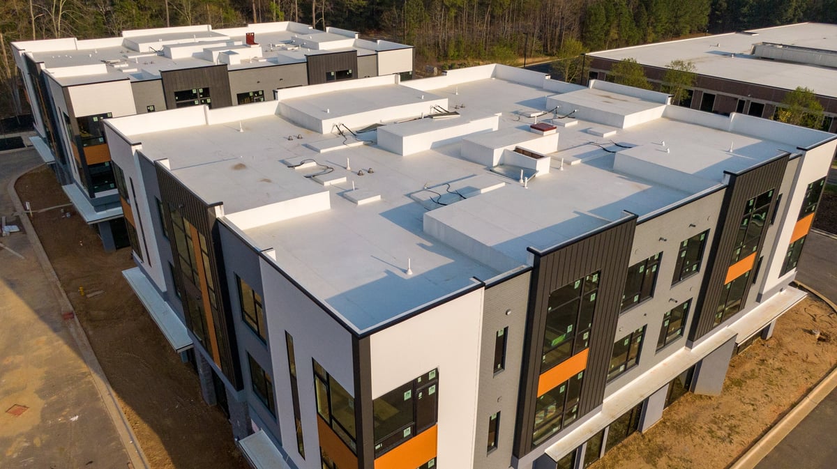 A high-resolution technical drone inspection photo of a commercial TPO roofing system showing critical installation details, heat-welded membrane seams and flashing around roof penetrations