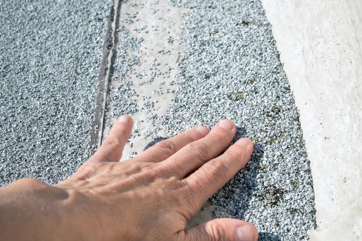 Bare spot on aged modified bitumen cap sheet at concrete parapet edge