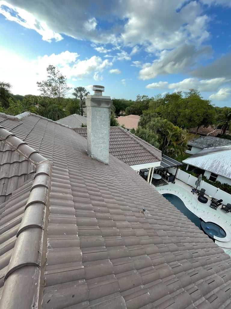 Roof view with gray ceramic tiles, white chimney, and lush green landscape under blue sky with clouds