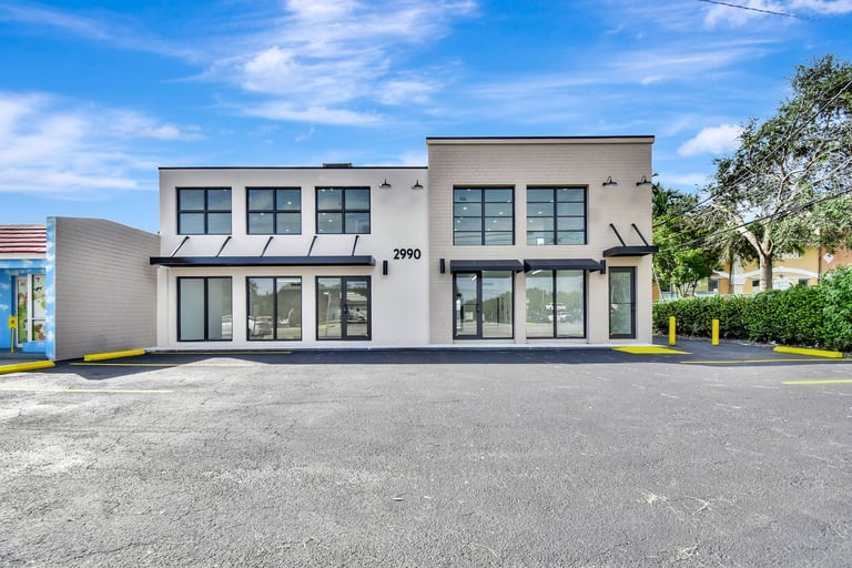 Modern commercial building with white exterior, large windows, and numbered address 2790 on a paved lot under blue sky